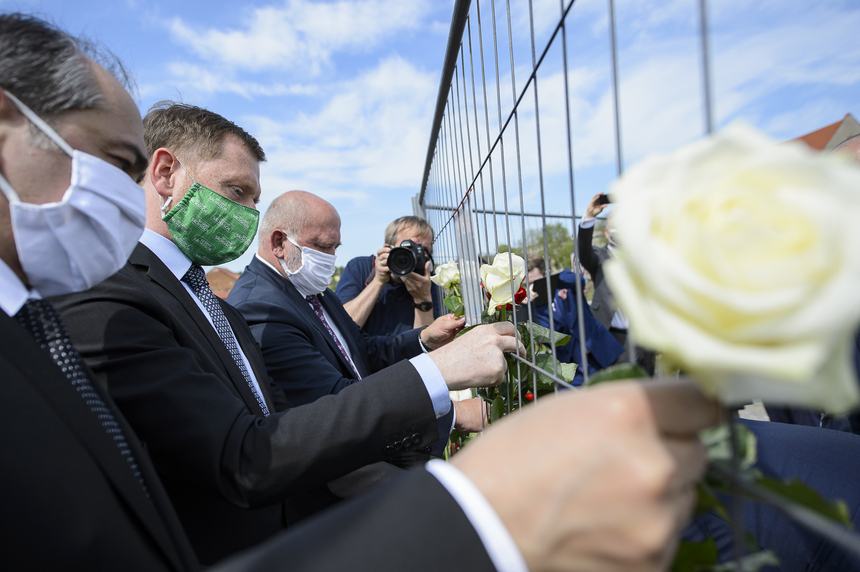 Männer mit Masken im Gesicht bringen an einem Bauzaun Rosen an.